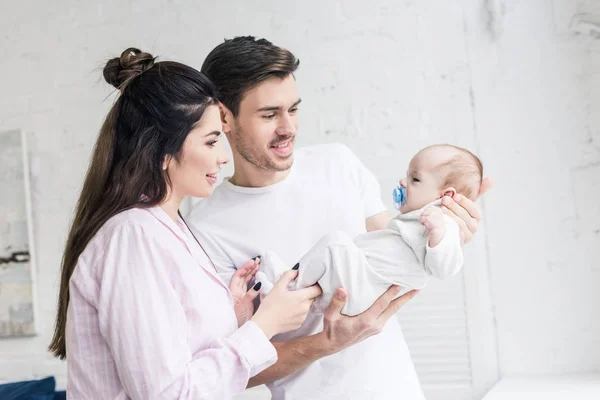 Side view of happy parents looking at little son with pacifier at home — Stock Photo