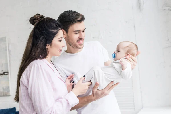 Vista laterale di genitori felici guardando il piccolo figlio con ciuccio a casa — Foto stock