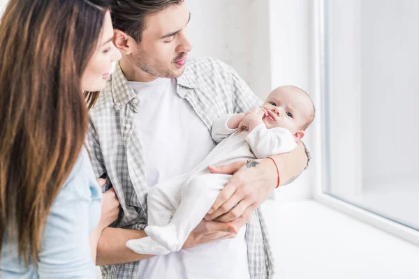 Selective focus of young mother and father looking at baby in hands at home — Stock Photo