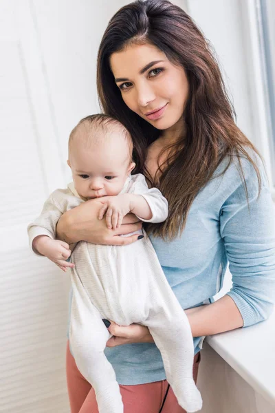 Porträt einer schönen jungen Mutter, die ihren kleinen Sohn zu Hause in den Händen hält — Stockfoto