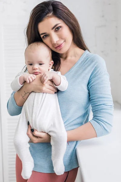 Retrato de bela jovem mãe segurando pequeno filho em mãos em casa — Fotografia de Stock