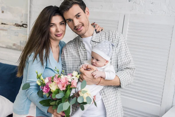 Portrait of happy parents with little son and bouquet of flowers at home — Stock Photo