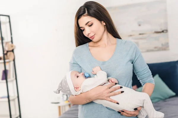 Retrato de la joven madre mirando al pequeño bebé en las manos en casa - foto de stock
