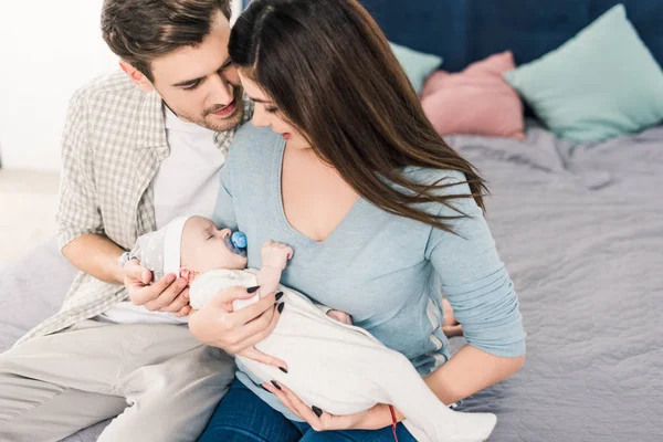 Portrait of young parents with cute baby sitting on bed at home — Stock Photo