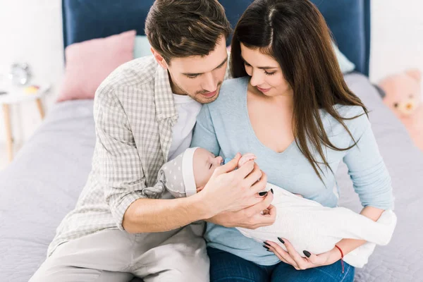 Retrato de padres jóvenes con lindo bebé sentado en la cama en casa - foto de stock