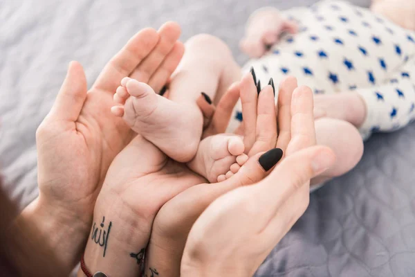 Vue partielle des parents tenant de petits bébés pieds dans les mains ensemble — Photo de stock