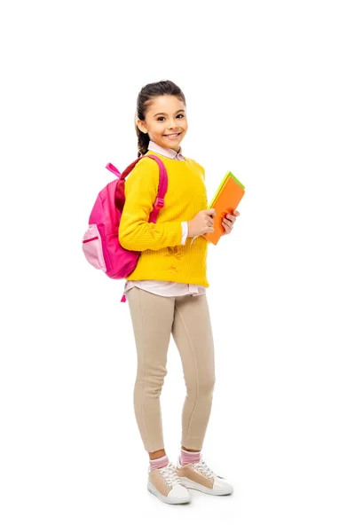 Adorable kid with backpack holding books while looking at camera isolated on white — Stock Photo