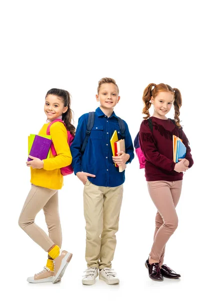 Lindos escolares con mochilas sosteniendo libros y sonriendo aislados en blanco - foto de stock
