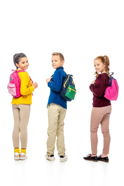 Escolares bonitos mostrando mochilas enquanto olha para a câmera isolada no branco — Fotografia de Stock