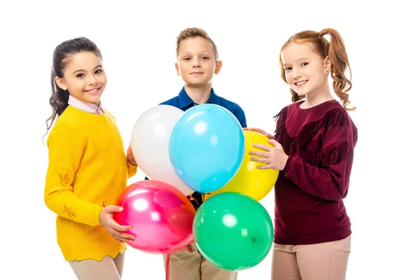 Niño sonriente y colegialas sosteniendo globos de colores y mirando a la cámara aislada en blanco - foto de stock