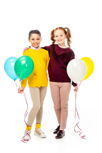 Colegialas sonrientes sosteniendo globos de colores y mirando a la cámara aislada en blanco - foto de stock