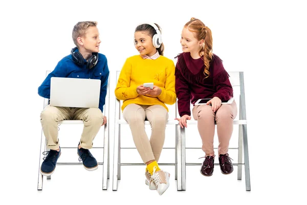 Écolières mignonnes avec des appareils numériques regardant garçon avec ordinateur portable isolé sur blanc — Photo de stock