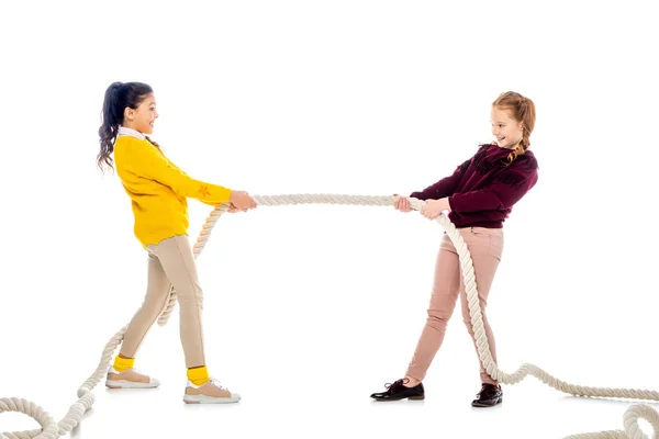 Two cheerful schoolgirls pulling rope and looking at each other isolated on white — Stock Photo