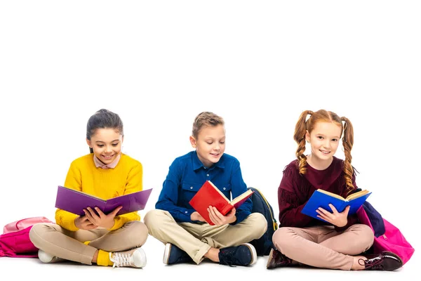 Lächelnde Schulkinder sitzen und lesen Bücher mit bunten Einbänden auf weißem Hintergrund. — Stockfoto