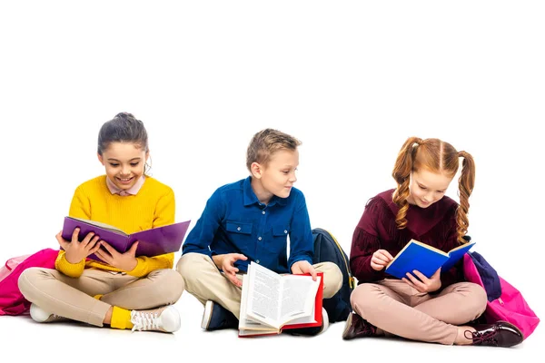 Des écoliers joyeux assis et lisant des livres isolés sur blanc — Stock Photo