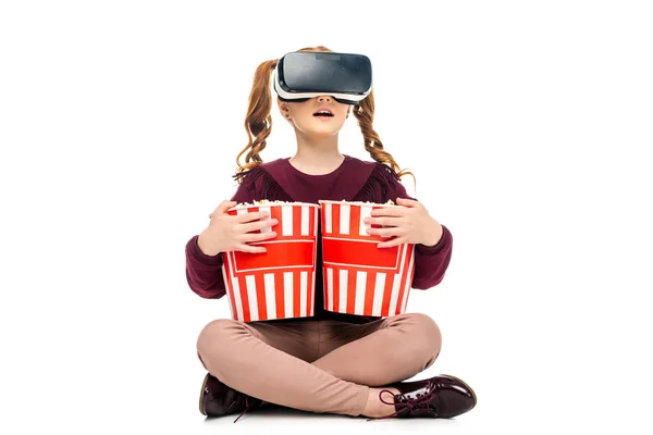 Bambino sorpreso con auricolare realtà virtuale sulla testa che tiene secchi di popcorn isolati su bianco — Foto stock