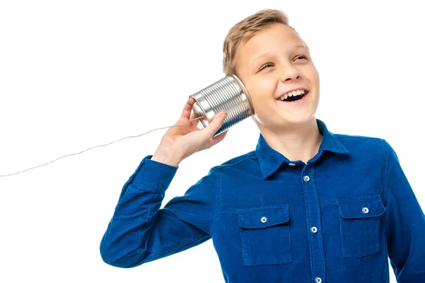 Niño sonriente sosteniendo estaño con cuerda cerca de la oreja aislado en blanco - foto de stock