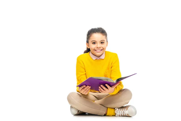 Весела школярка тримає фіолетову книгу і дивиться на камеру ізольовано на білому — стокове фото
