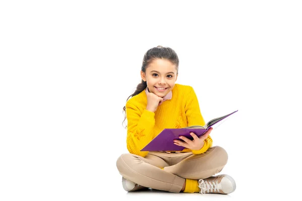 Colegiala sonriente en suéter amarillo sosteniendo libro púrpura y mirando a la cámara aislada en blanco - foto de stock
