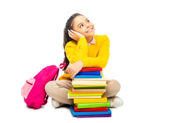Мечтательная школьница сидит около стопки книг и розовый рюкзак изолирован на белом — стоковое фото