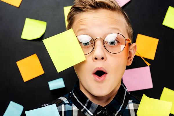 Nahaufnahme eines überraschten Jungen in Brille mit bunten Aufklebern, der in die Kamera auf schwarzem Hintergrund blickt — Stockfoto