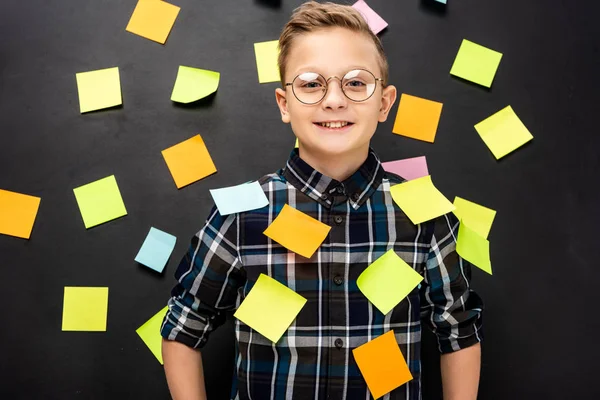 Smiling boy in glasses with multicolored stickers looking at camera on black background — Stock Photo
