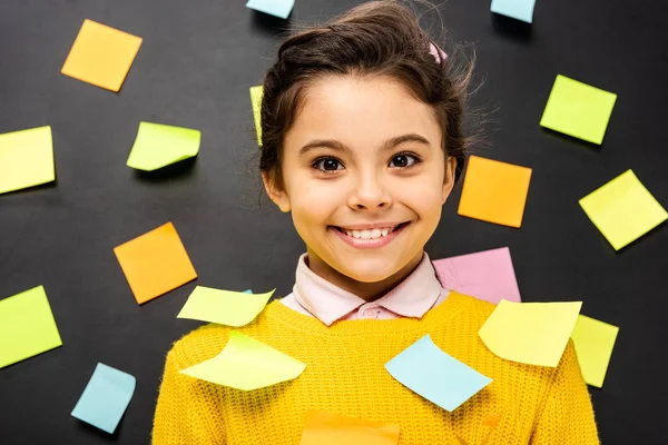 Cheerful schoolgirl in yellow sweater with multicolored stickers looking at camera on black background — Stock Photo