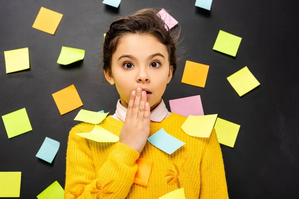 Surprised schoolgirl with multicolored stickers looking at camera on black background — Stock Photo