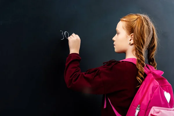 Schoolgirl with pink backpack writing on blackboard with chalk — Stock Photo