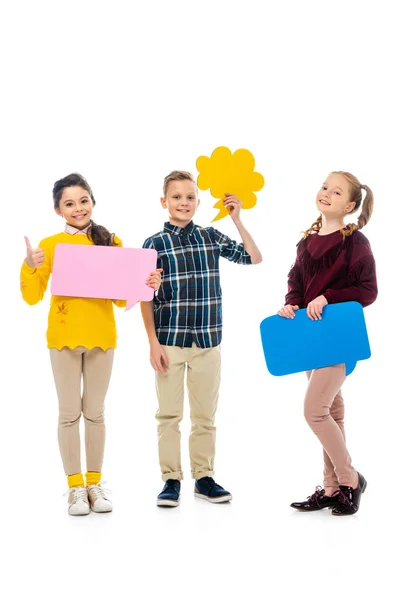 Niños alegres sosteniendo burbujas de habla multicolores, mostrando el pulgar hacia arriba y mirando a la cámara aislada en blanco - foto de stock