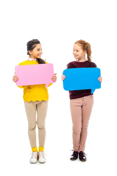 Colegialas alegres sosteniendo burbujas de habla multicolores y mirándose aislados en blanco - foto de stock