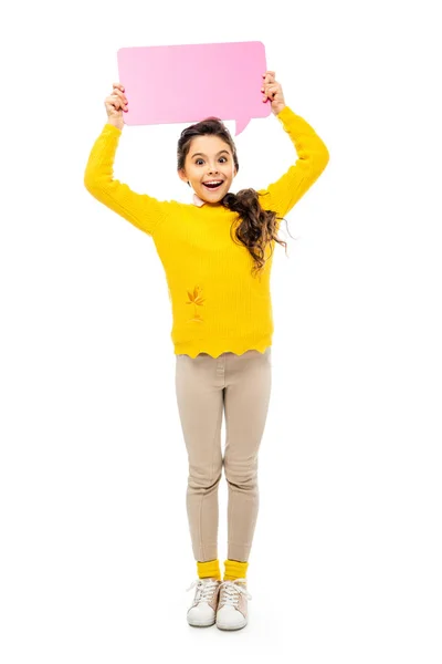 Cheerful schoolgirl in yellow sweater holding pink speech bubble over head and looking at camera isolated on white — Stock Photo