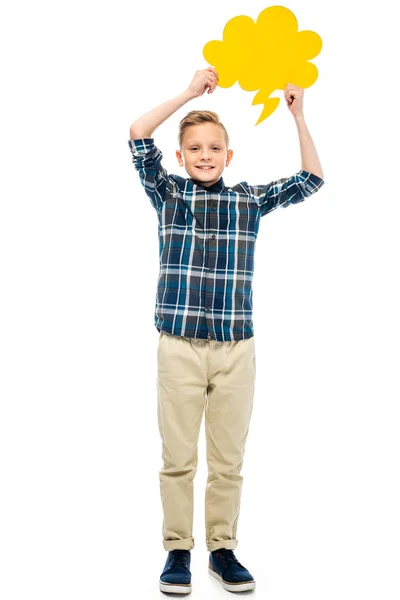 Niño sonriente sosteniendo burbuja de habla amarilla sobre la cabeza y mirando a la cámara aislada en blanco - foto de stock