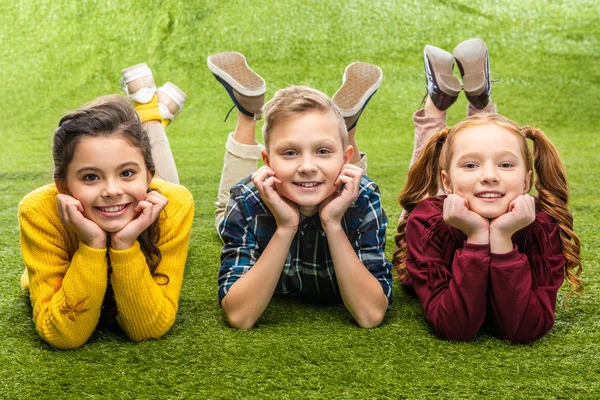 Lächelnde Kinder, die auf dem Rasen liegen und in die Kamera schauen — Stockfoto