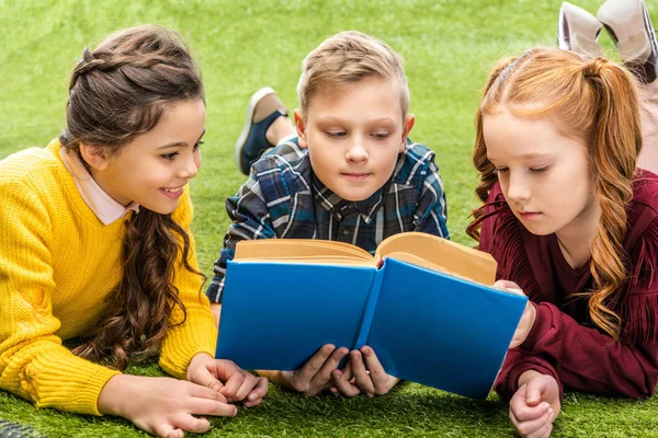 Crianças bonitos deitado no gramado e livro de leitura — Fotografia de Stock