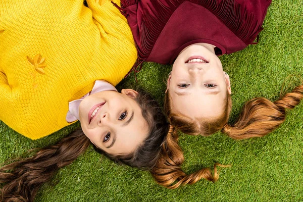 Top view of smiling schoolgirls lying head to head on lawn — Stock Photo