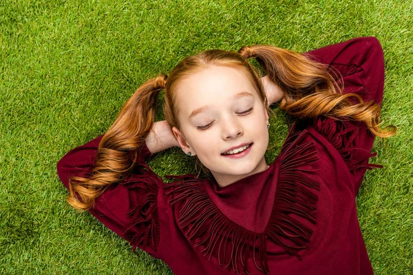 Vue de dessus de l'écolière mignonne couchée sur la pelouse avec les yeux fermés — Photo de stock