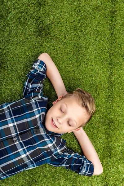 Draufsicht des niedlichen Jungen, der mit geschlossenen Augen auf dem Rasen liegt — Stockfoto