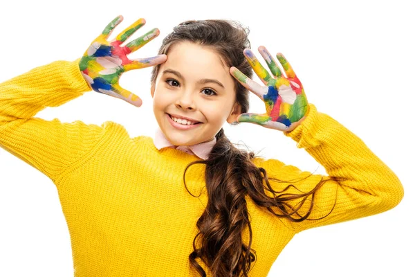Écolière souriante en pull jaune regardant la caméra et montrant les mains peintes dans des peintures colorées isolées sur blanc — Photo de stock