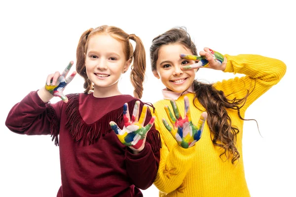 Smiling schoolgirls showing peace signs with hands painted in colorful paints and looking at camera isolated on white — Stock Photo