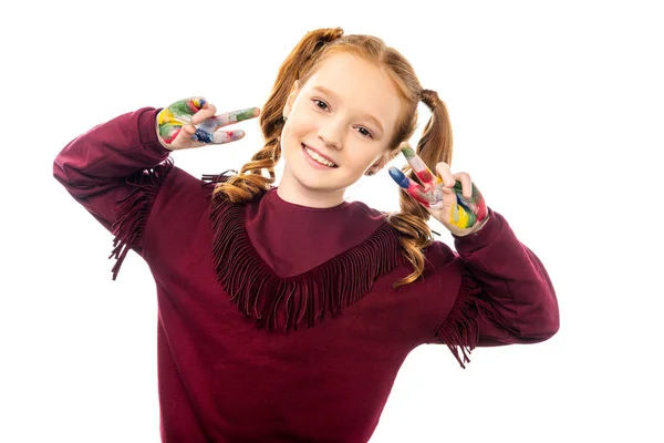 Smiling schoolgirl looking at camera and showing peace signs with hands painted in colorful paints isolated on white — Stock Photo