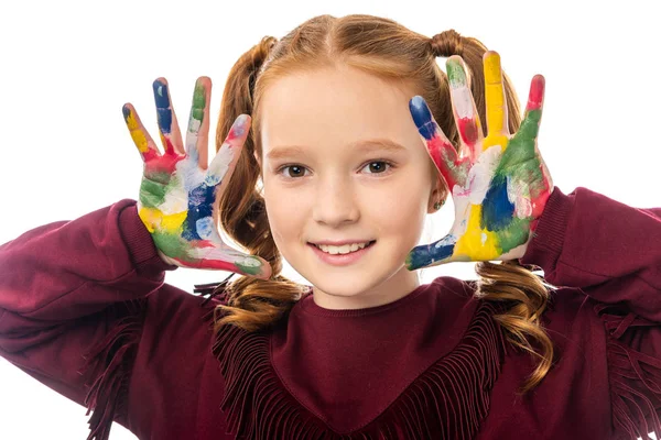 Vue rapprochée de l'écolière mignonne regardant la caméra et montrant les mains peintes dans des peintures colorées isolées sur blanc — Photo de stock