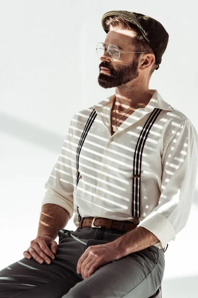 Schöner bärtiger Mann mit Brille und Mütze sitzt auf weißem Hintergrund — Stockfoto
