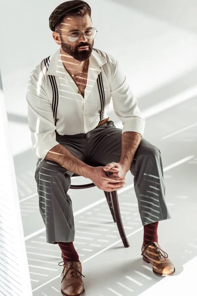 Handsome bearded man with clenched hands sitting on chair and looking at camera — Stock Photo