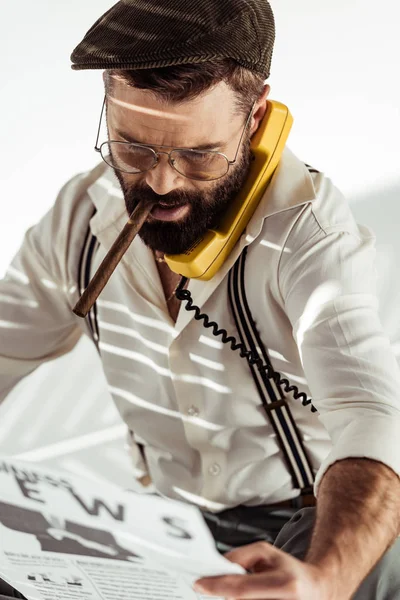 Homem barbudo em óculos e boné falando no telefone vintage, fumar charuto e ler jornal — Fotografia de Stock