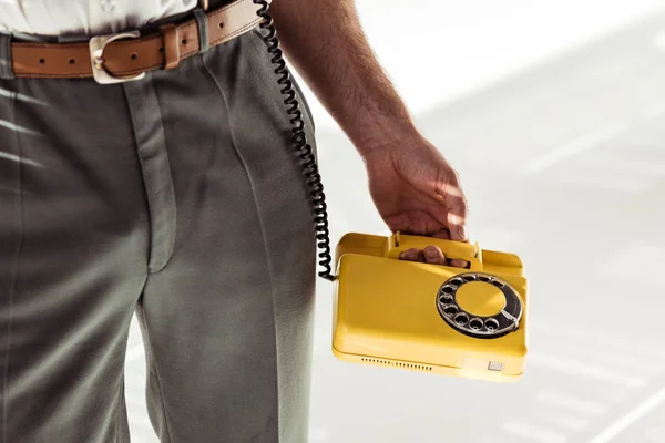 Vista ritagliata di uomo in possesso retrò giallo telefono su sfondo bianco — Foto stock