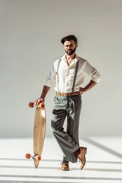 Handsome bearded man holding longboard and looking at camera on grey background — Stock Photo