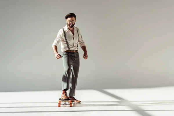 Handsome bearded man riding longboard and looking at camera on grey background — Stock Photo