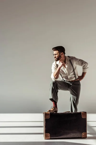 Hombre barbudo guapo cerca de maleta retro sobre fondo gris - foto de stock