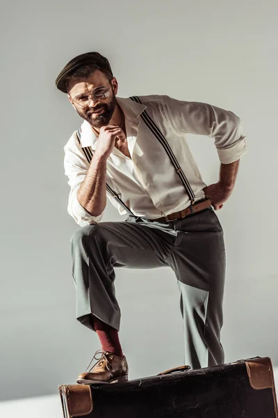 Handsome bearded man near retro suitcase smiling and looking at camera on grey background — Stock Photo